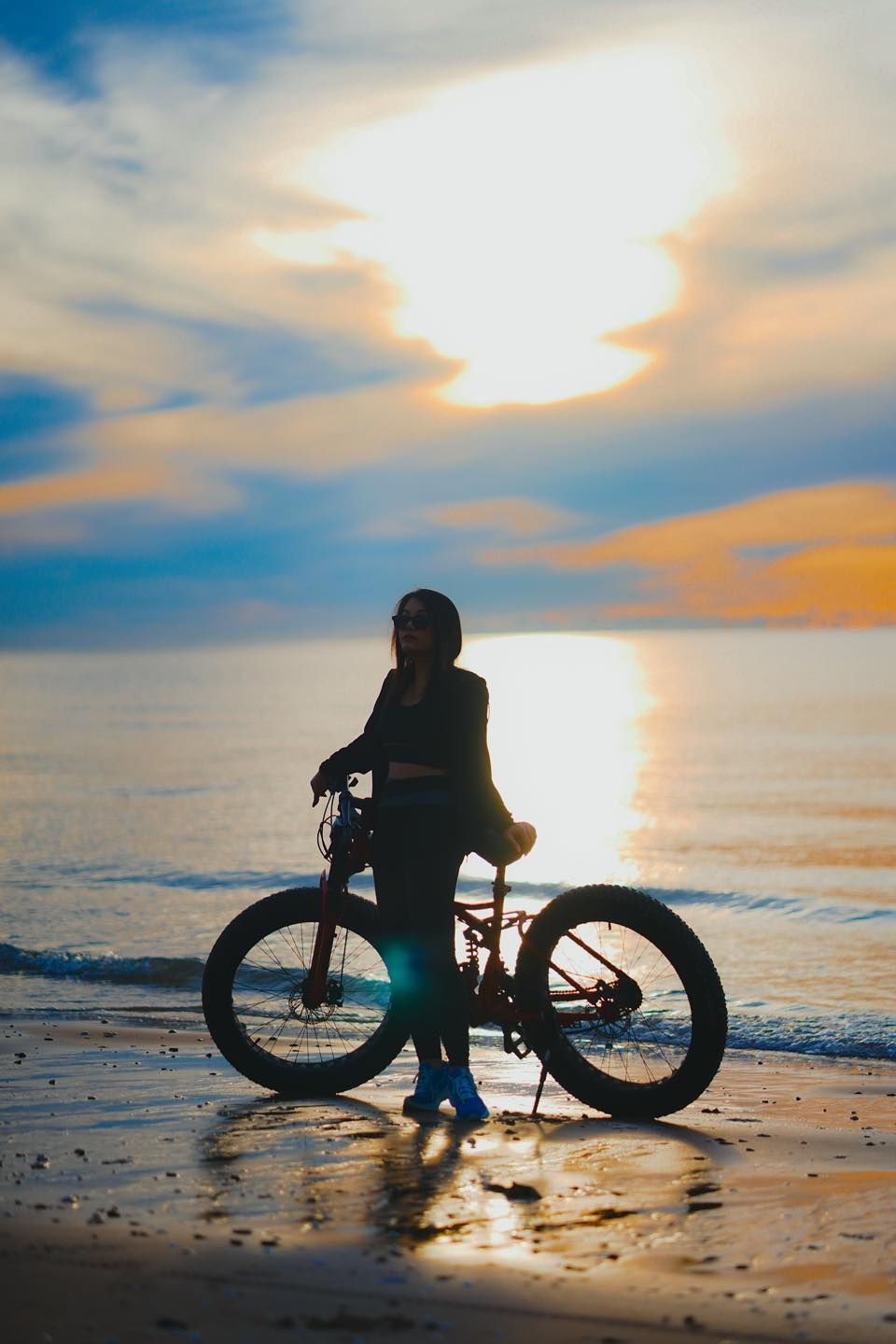 A woman is riding a bike on the beach at sunset.