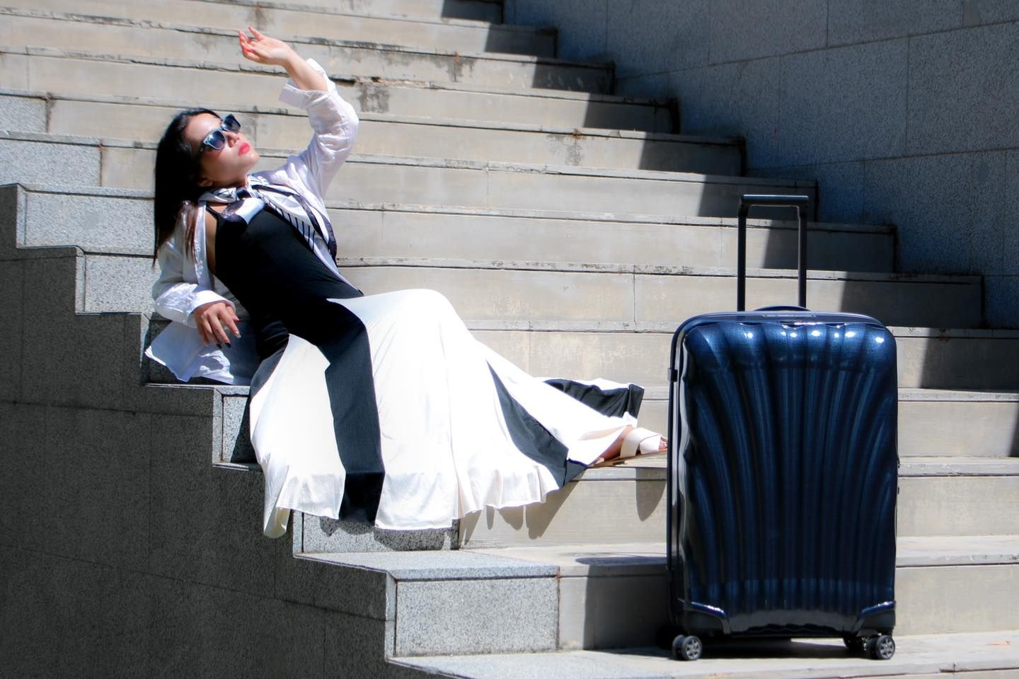 A woman is sitting on a set of stairs next to a suitcase