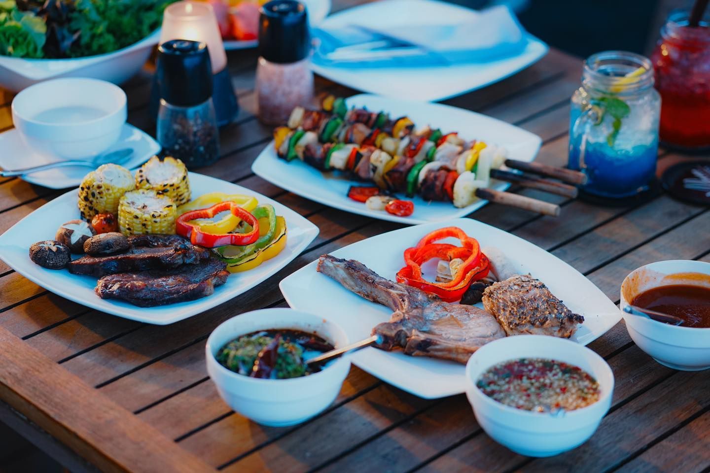 A wooden table topped with plates of food and bowls of sauce.