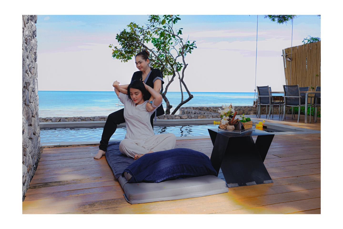 A woman is giving a massage to another woman in a room with a view of the ocean.