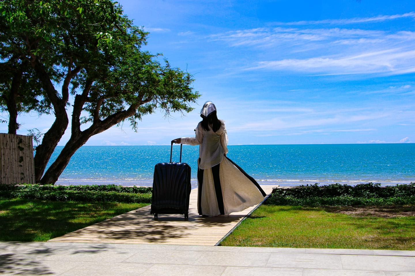 A woman is standing next to a suitcase looking at the ocean.