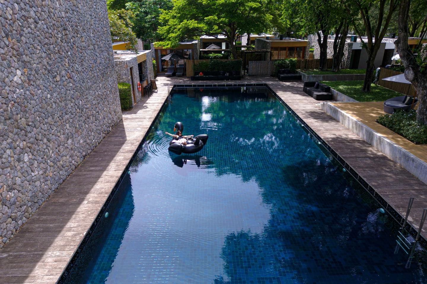 A large swimming pool surrounded by trees and a stone wall.