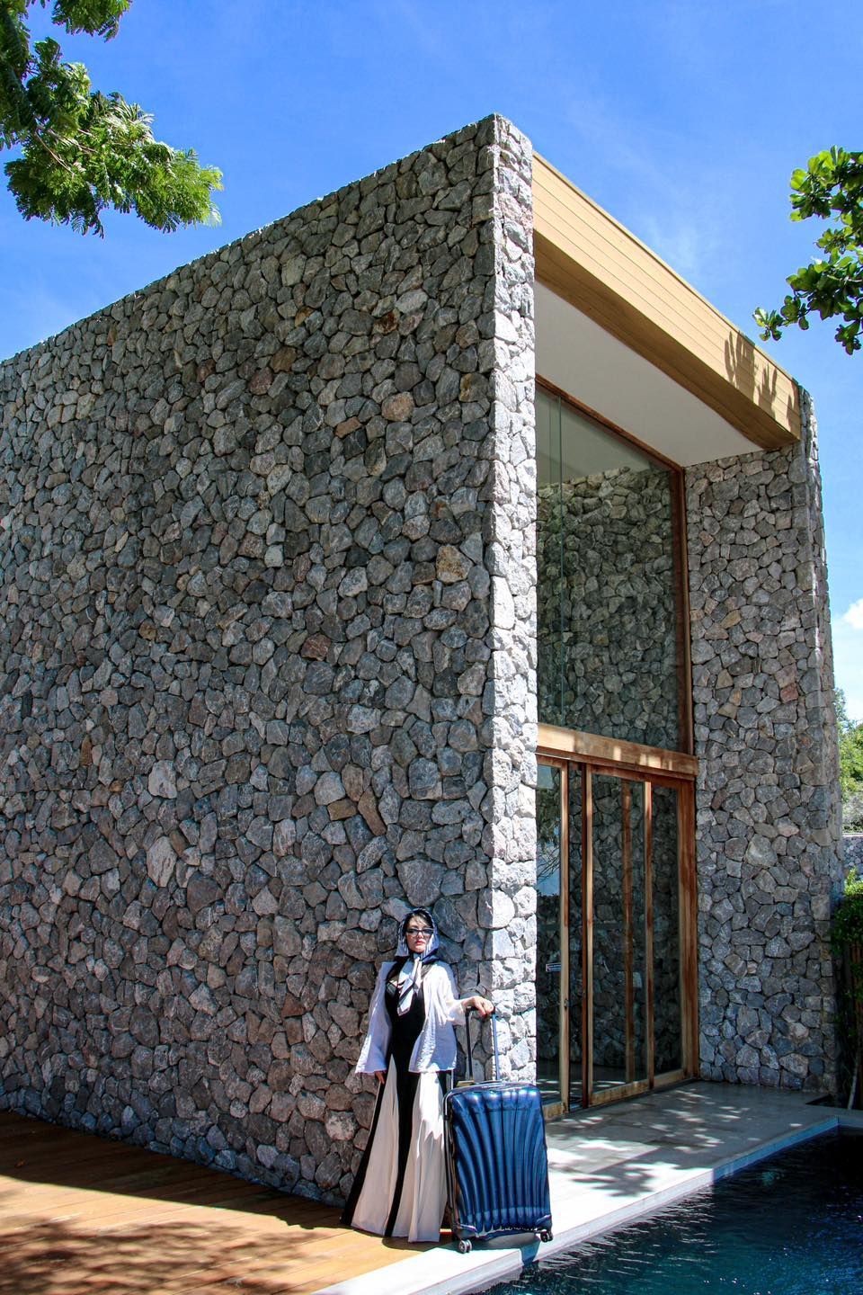 A woman is standing in front of a stone building holding the samsonite suitcase.