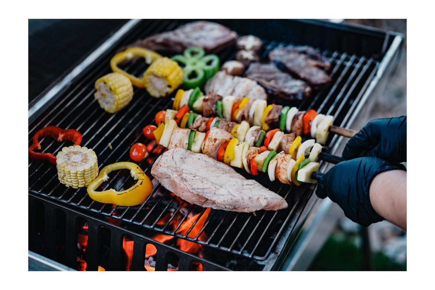 A person is cooking meat and vegetables on a grill.