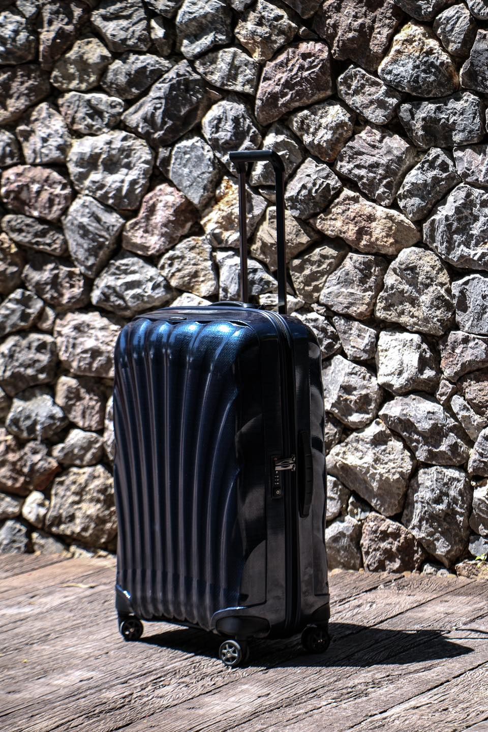 A samsonite suitcase is sitting on a wooden floor in front of a stone wall.