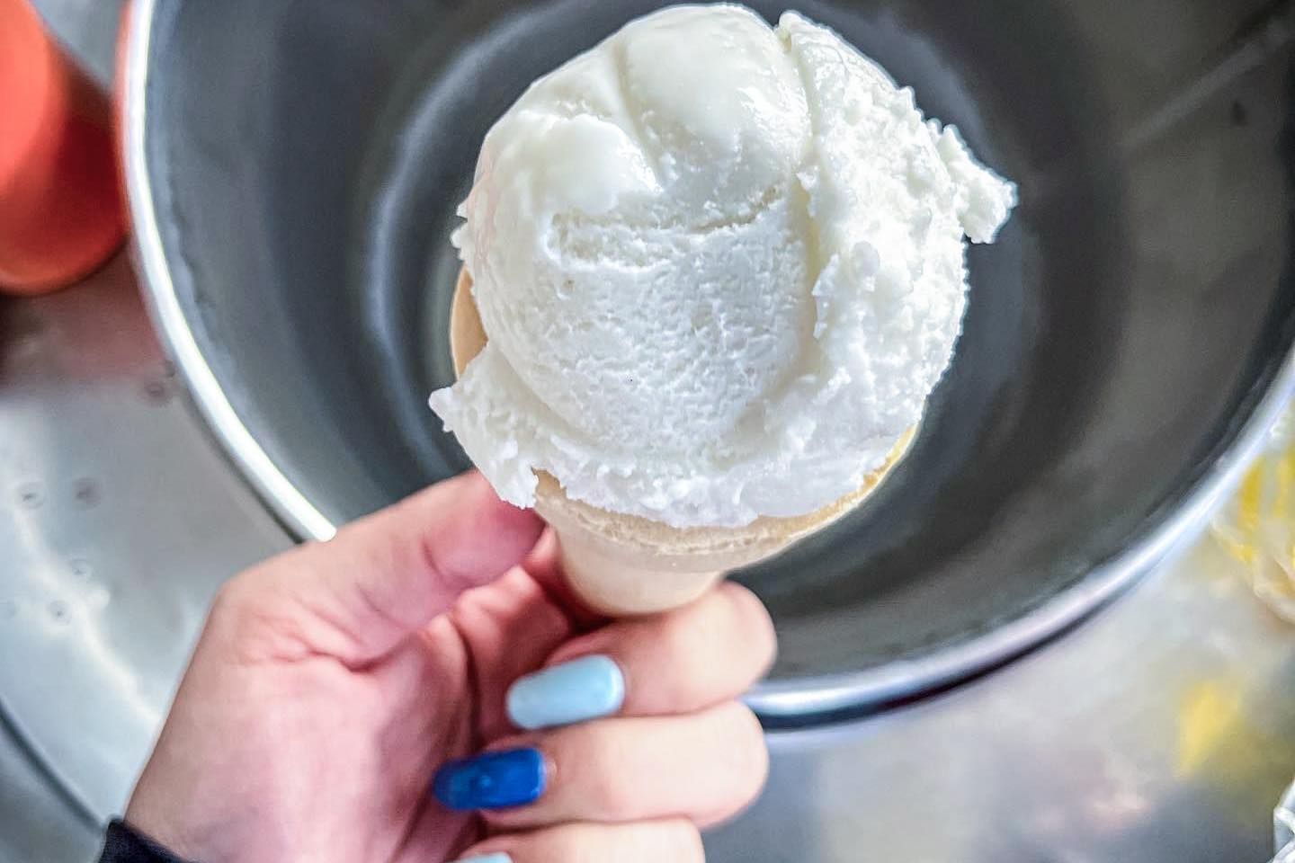 A person is holding a coconut ice cream cone in their hand.