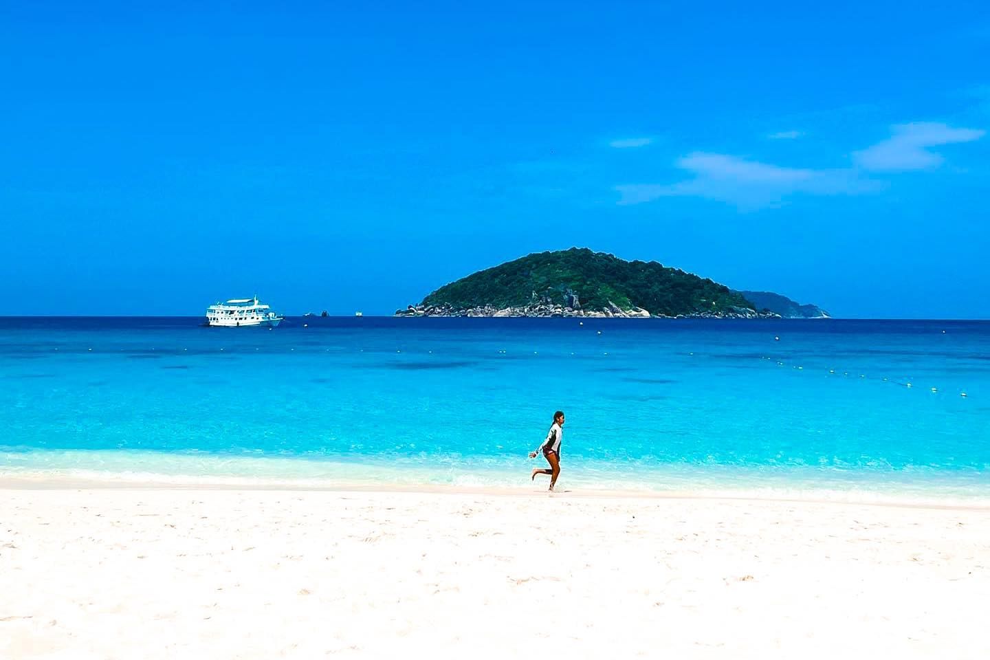 A woman is running on a beach with a boat in the background.