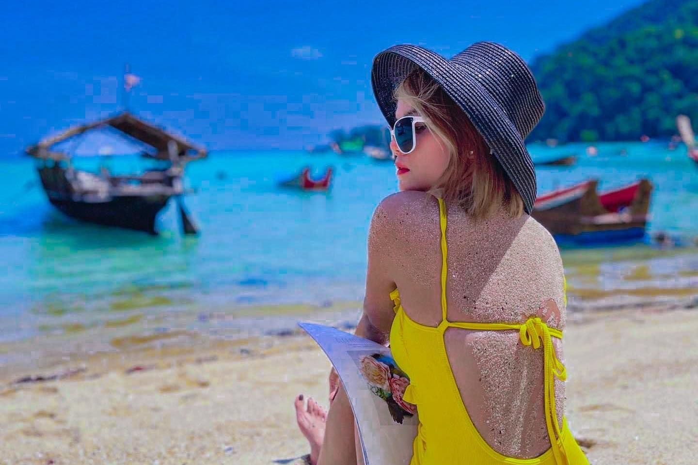 A woman in a yellow bikini and hat is sitting on the Surin Islands beach in Thailand.
