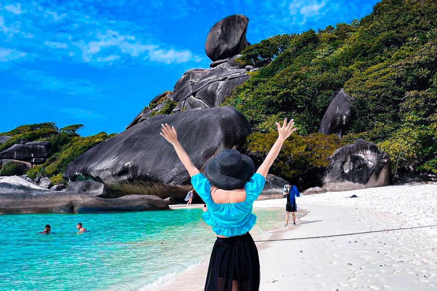 A woman is standing on a beach with her arms in the air.