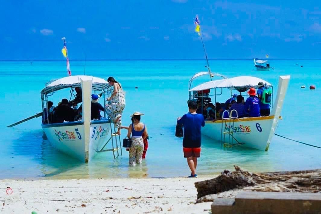 A man and a woman are walking towards two boats in the ocean.