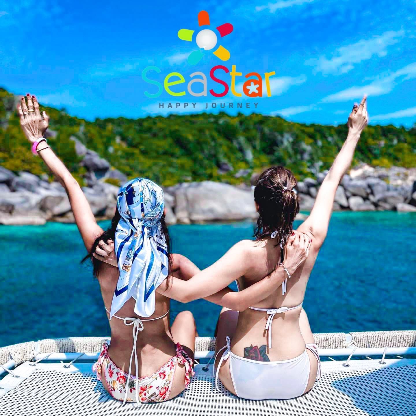 Two women in bikinis are sitting on a boat with their arms in the air.