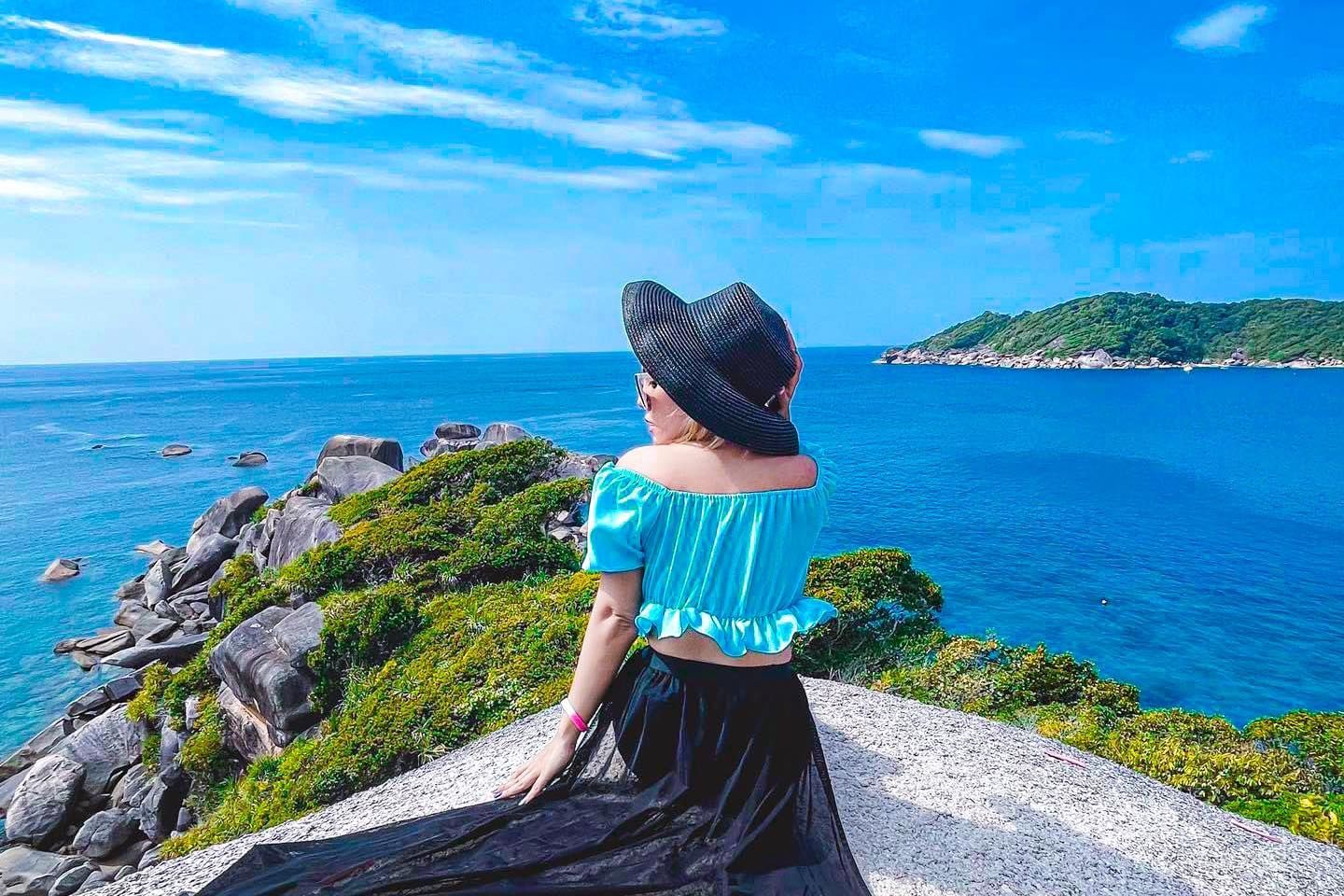 A woman is sitting on a cliff overlooking the ocean on similan islands.