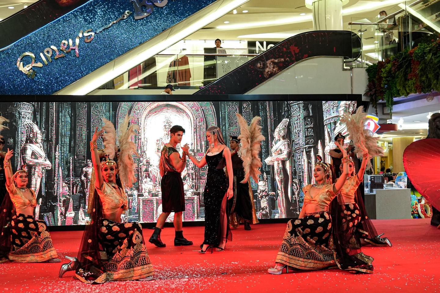A group of people are dancing on a red carpet in a mall.