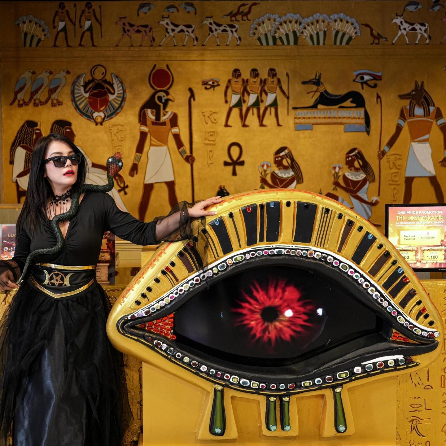 A woman in a black dress is standing next to a large eye