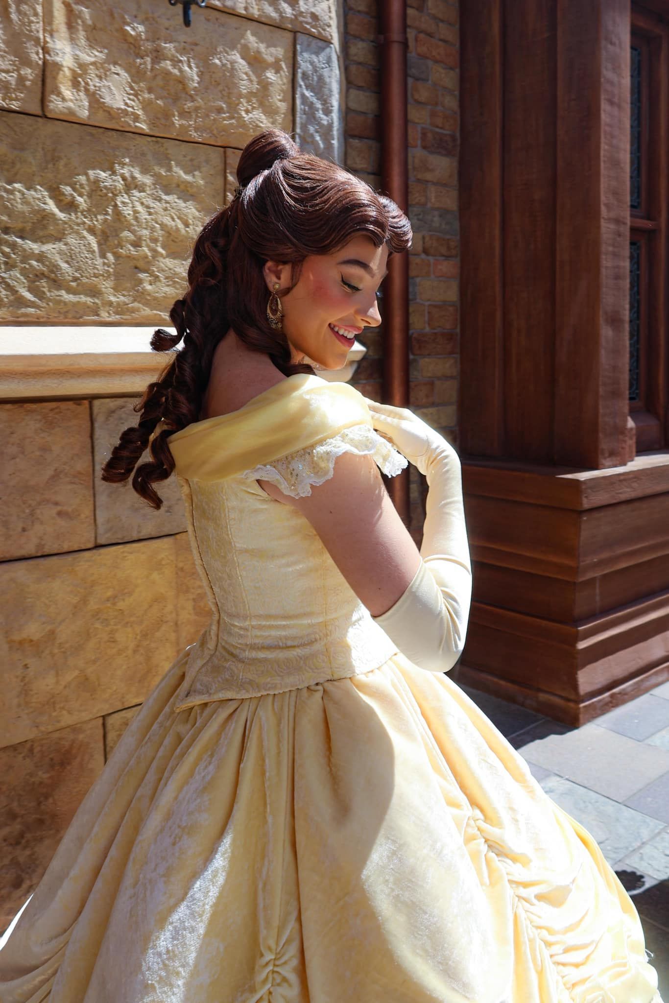 A woman named Belle in a yellow dress is standing in front of a building.