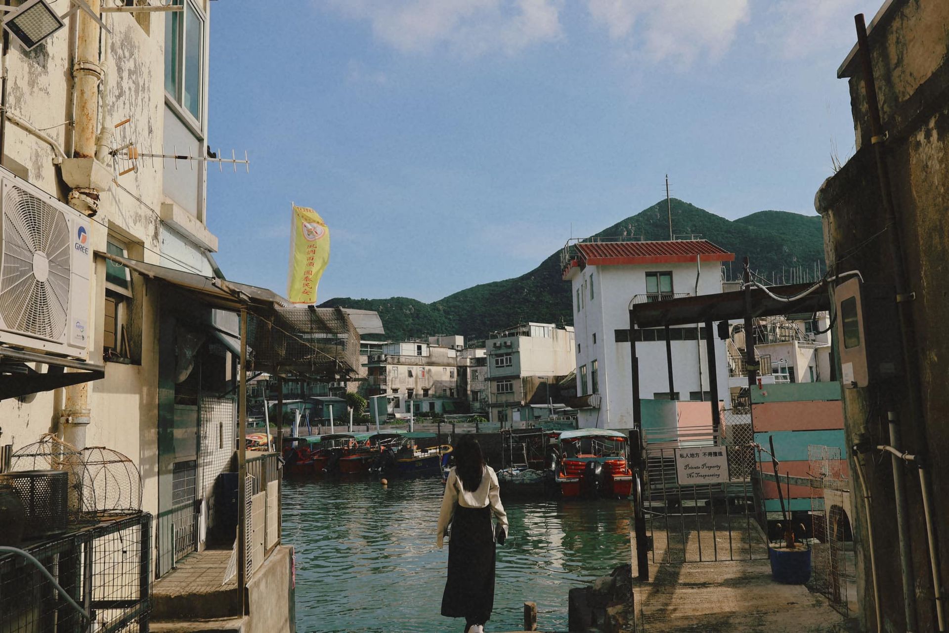 A woman is standing next to a body of water between two buildings in tai o fishing village.