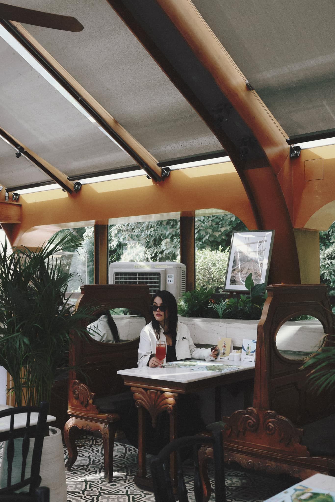 A woman sits at a table with a drink in her hand