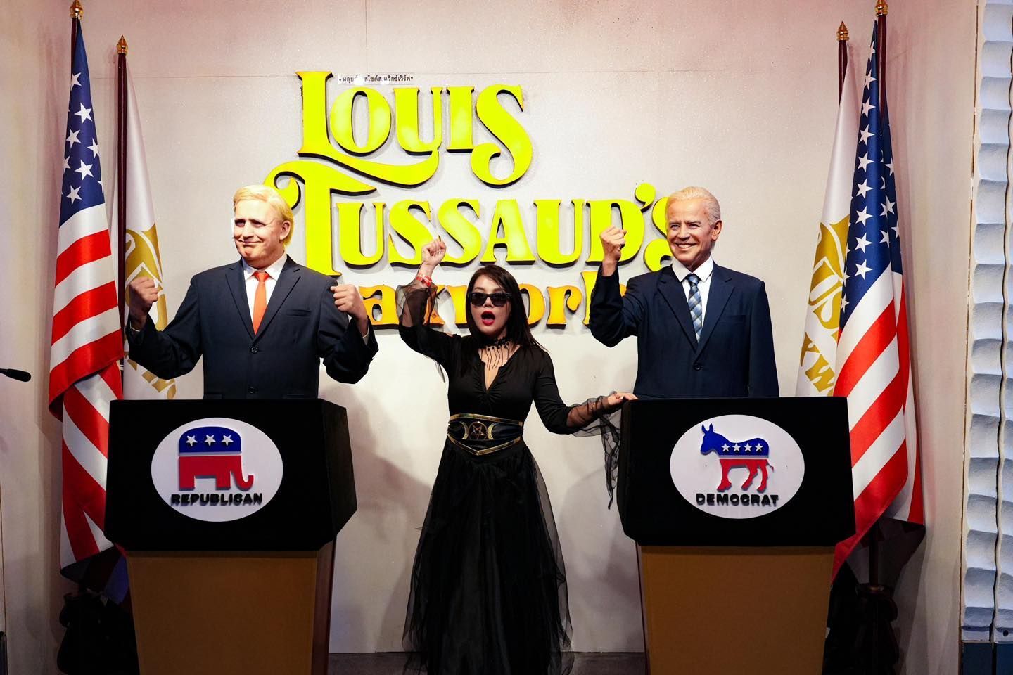 A woman in a black dress is standing between two statues of presidents made of  louis tussaud 's waxworks