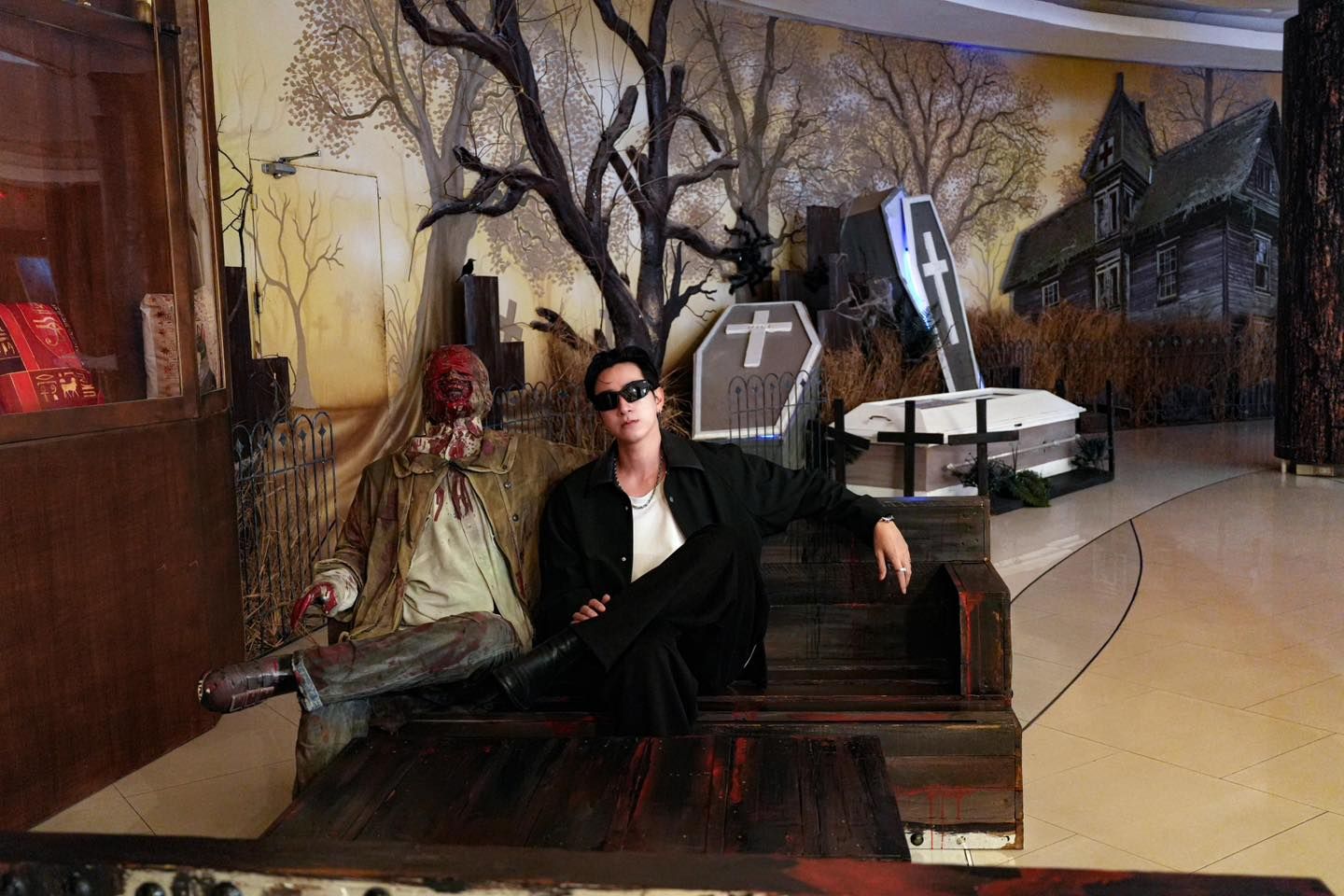 A man is sitting on a chair in front of a coffin with a cross on it.