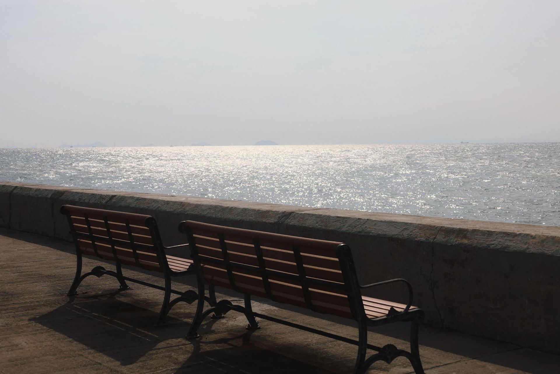 Two benches are sitting on a sidewalk overlooking the ocean.