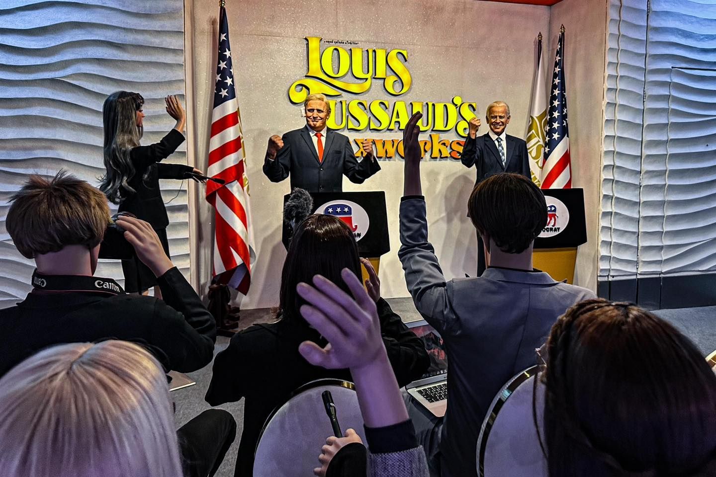 A group of people are raising their hands in front of a statue of  louis tussaud