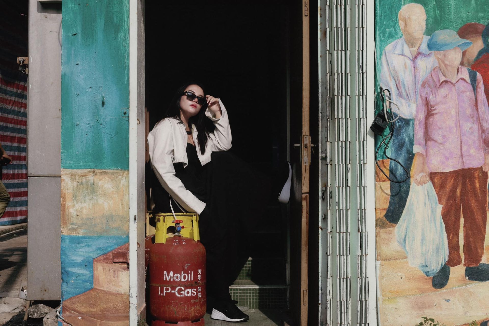 A woman is sitting in a doorway next to a propane tank.