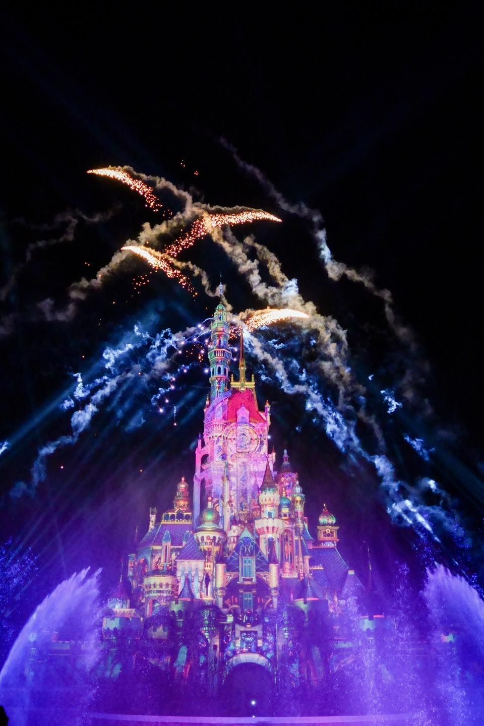 A castle is lit up at night with fireworks coming out of it.