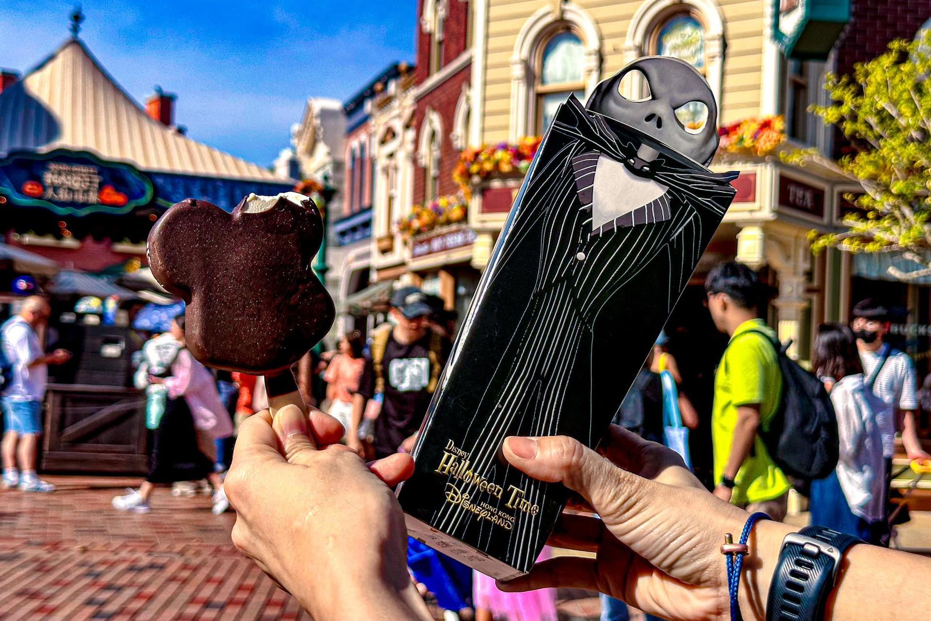 A person is holding a mickey mouse ice cream bar and a nightmare before christmas ice cream bar.