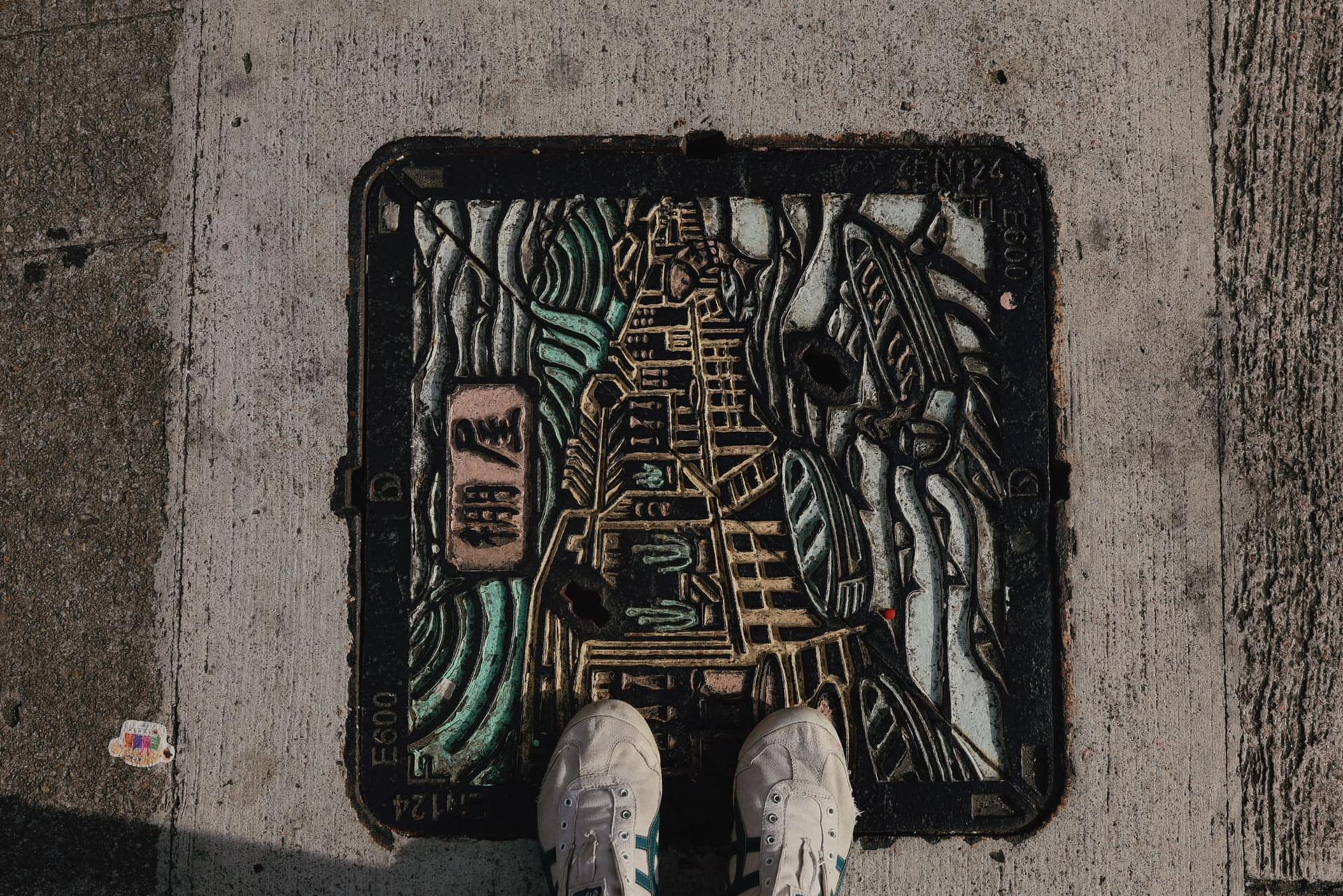 A person is standing on a manhole cover on the sidewalk.