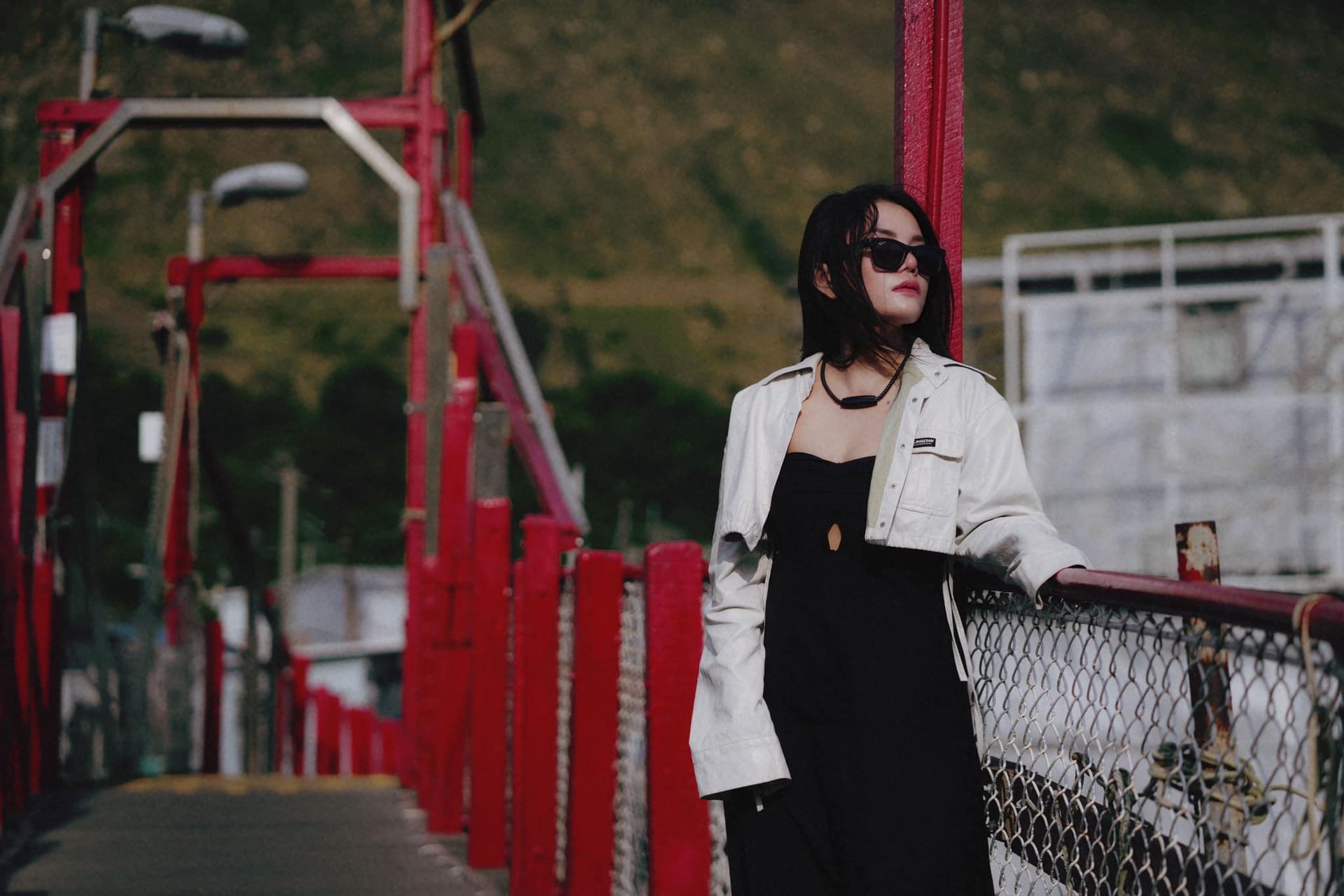 A woman in a black dress and white jacket is standing on a bridge.