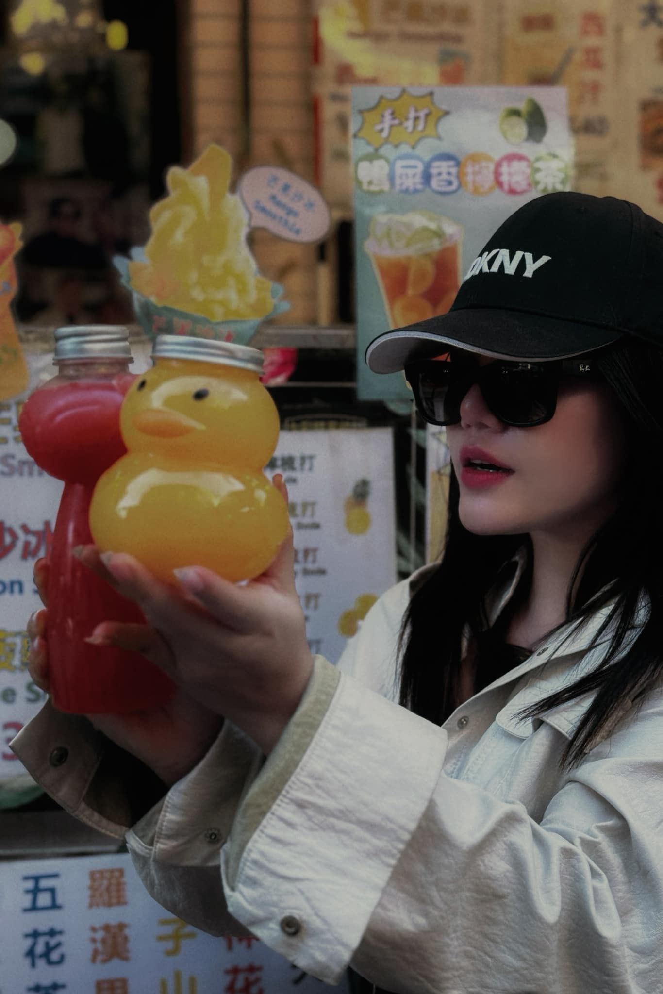A woman wearing a black hat and sunglasses is holding a rubber duck in her hand.