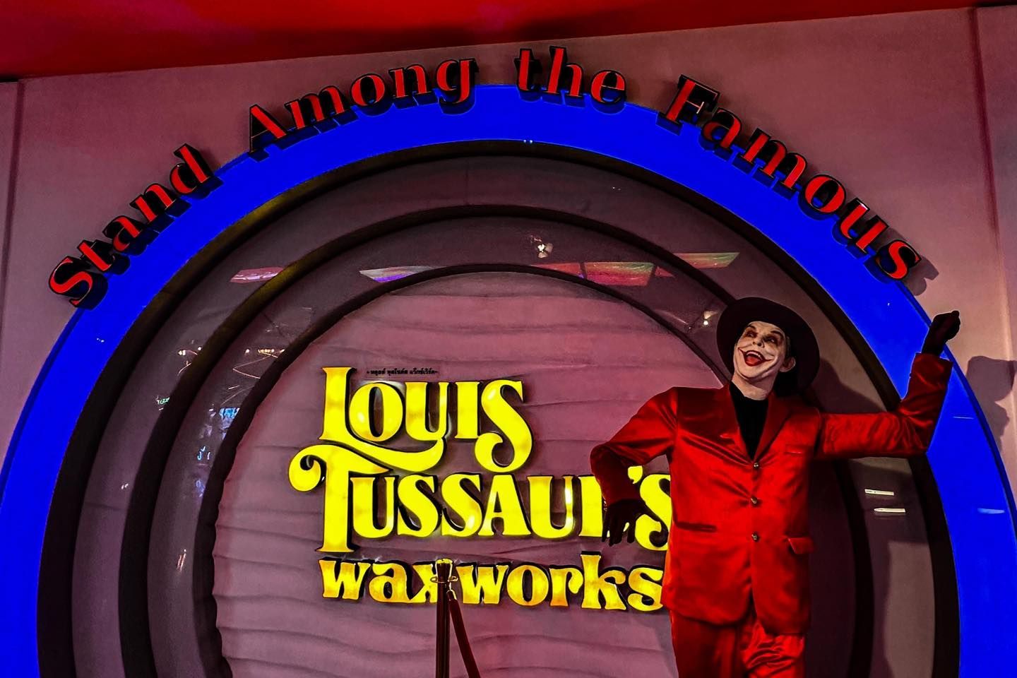 A man in a red suit is standing in front of a sign that says louis tussaud 's waxworks