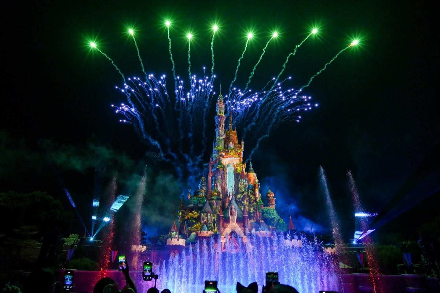 A group of people are taking pictures of fireworks over a castle.