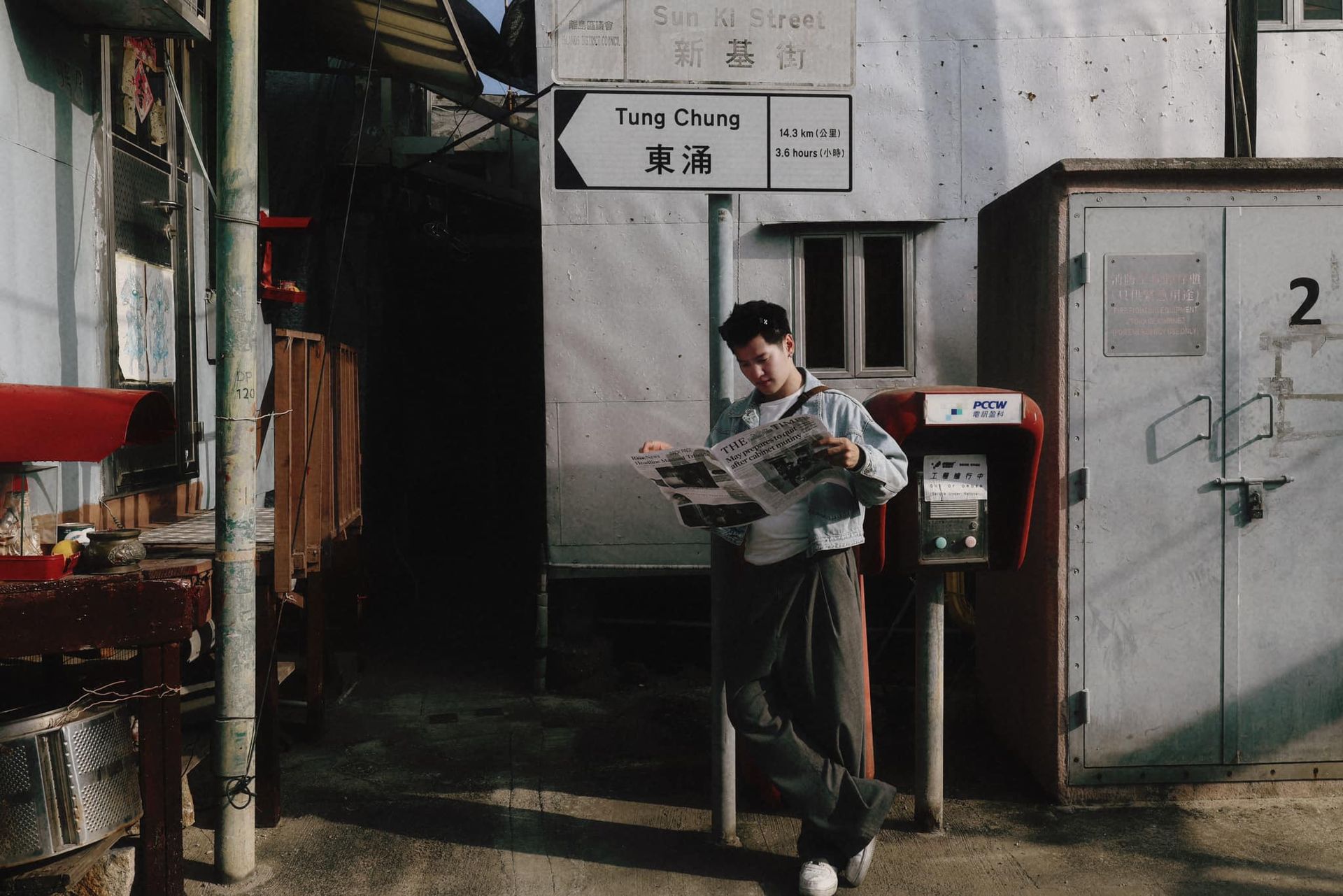 A man leans against a post box reading a newspaper