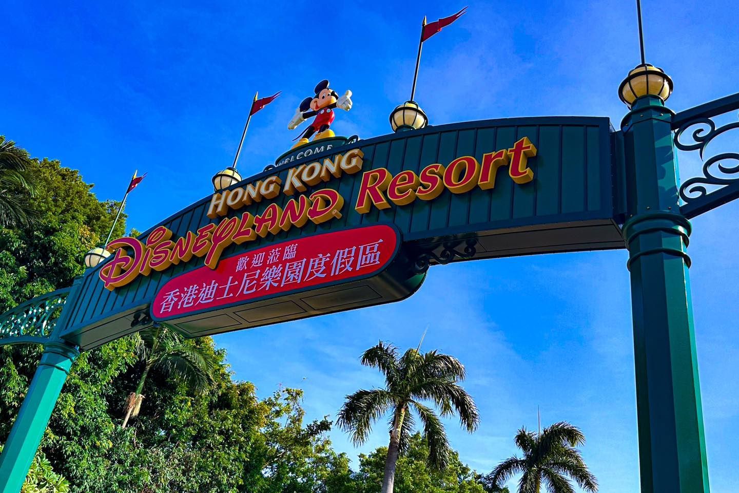 A sign for hong kong Disneyland resort is surrounded by palm trees