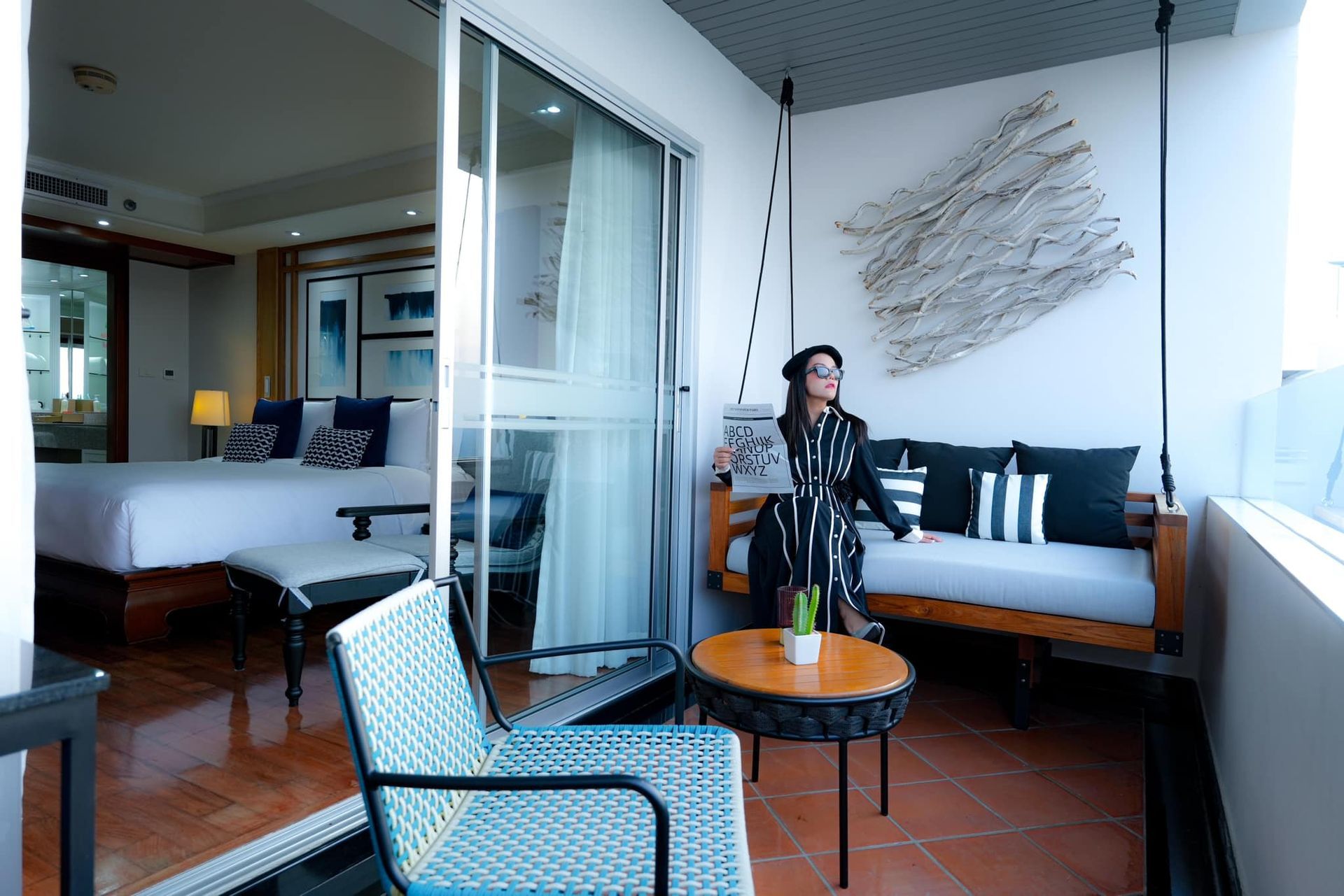 A woman is standing on a balcony in a hotel room holding a magazine.