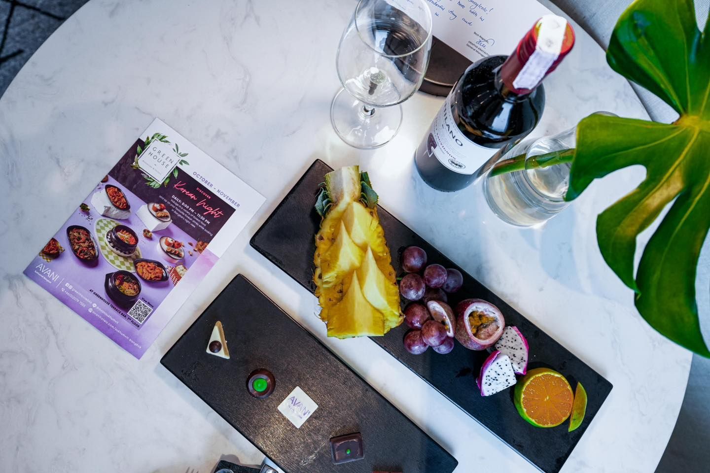 A table with a bottle of wine , a tray of fruit and a magazine.