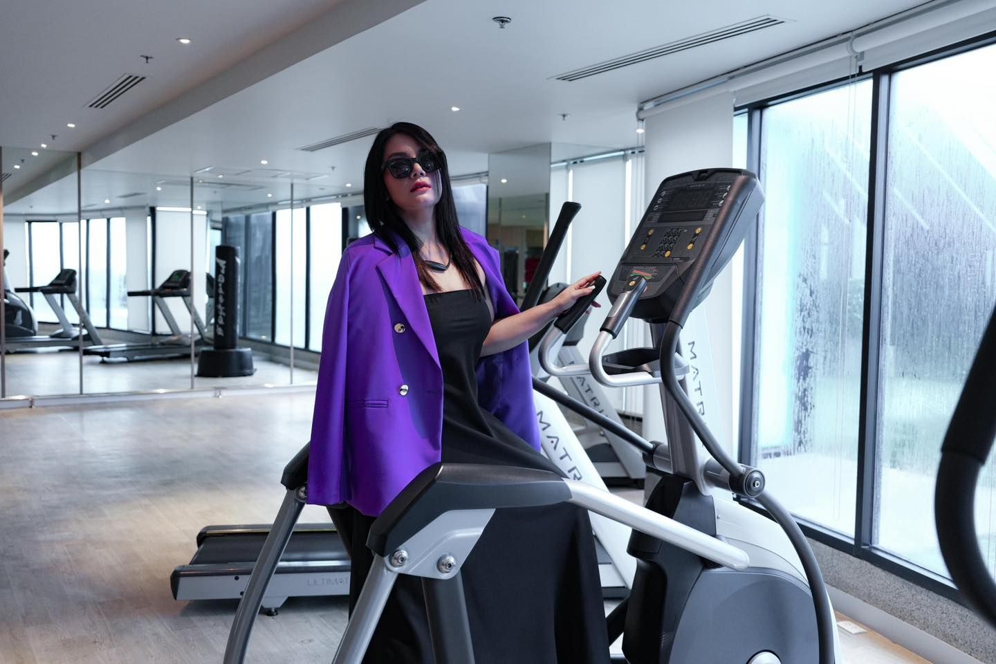A woman in a purple jacket is riding an elliptical machine in a gym.