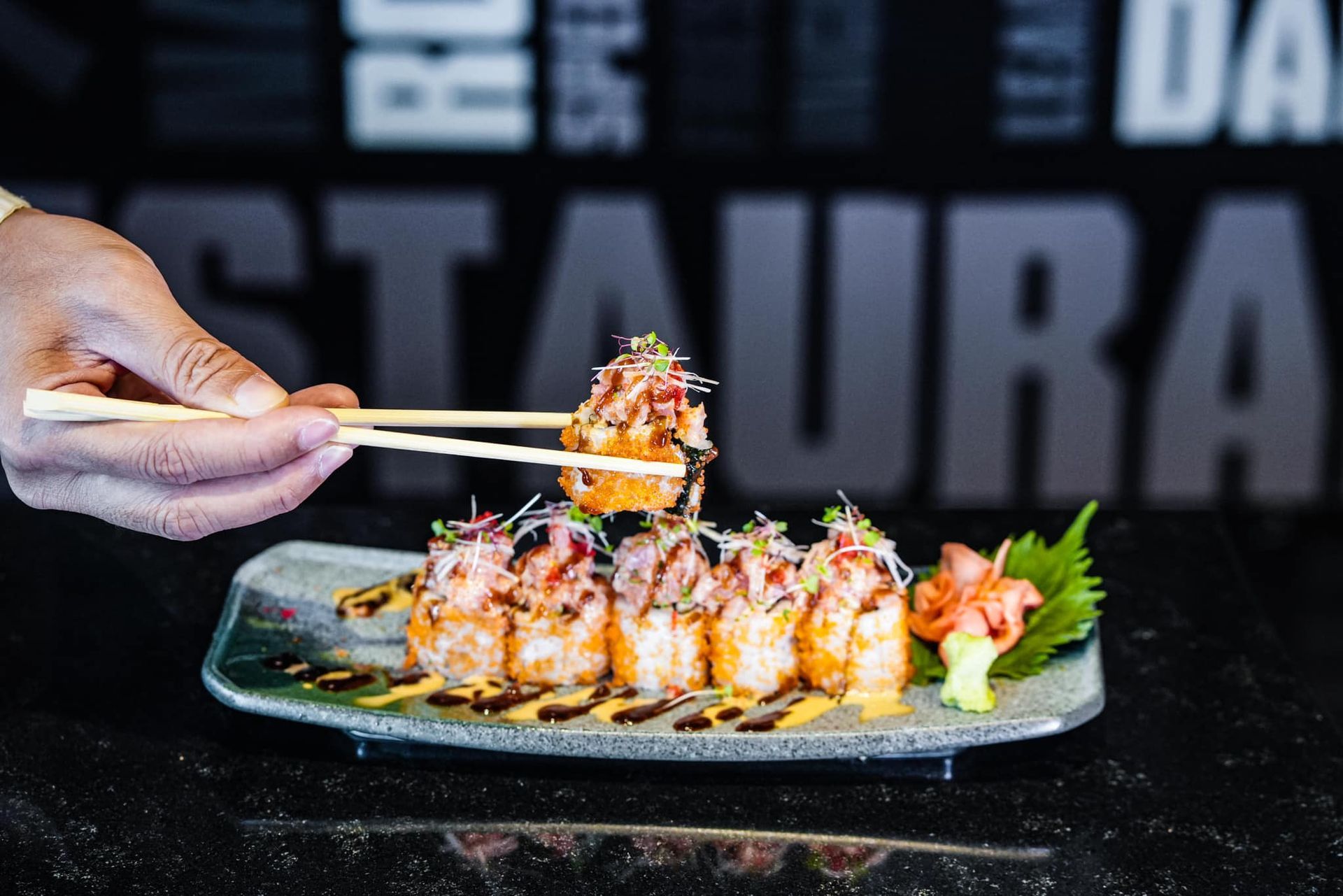 A person is holding chopsticks over a plate of sushi