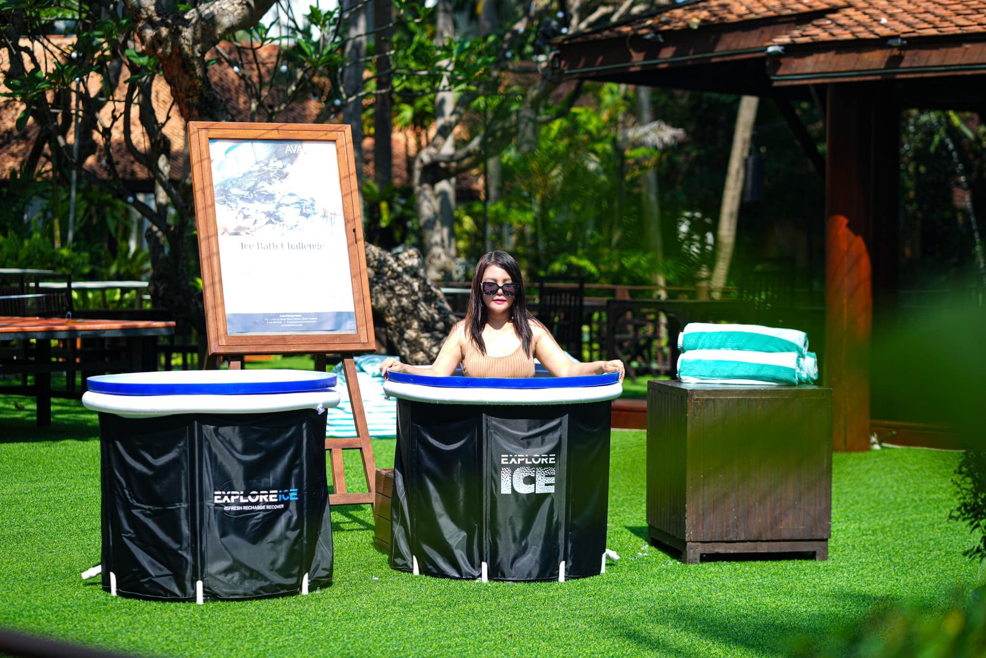 A woman is sitting in an inflatable tub of ice on a lush green field.