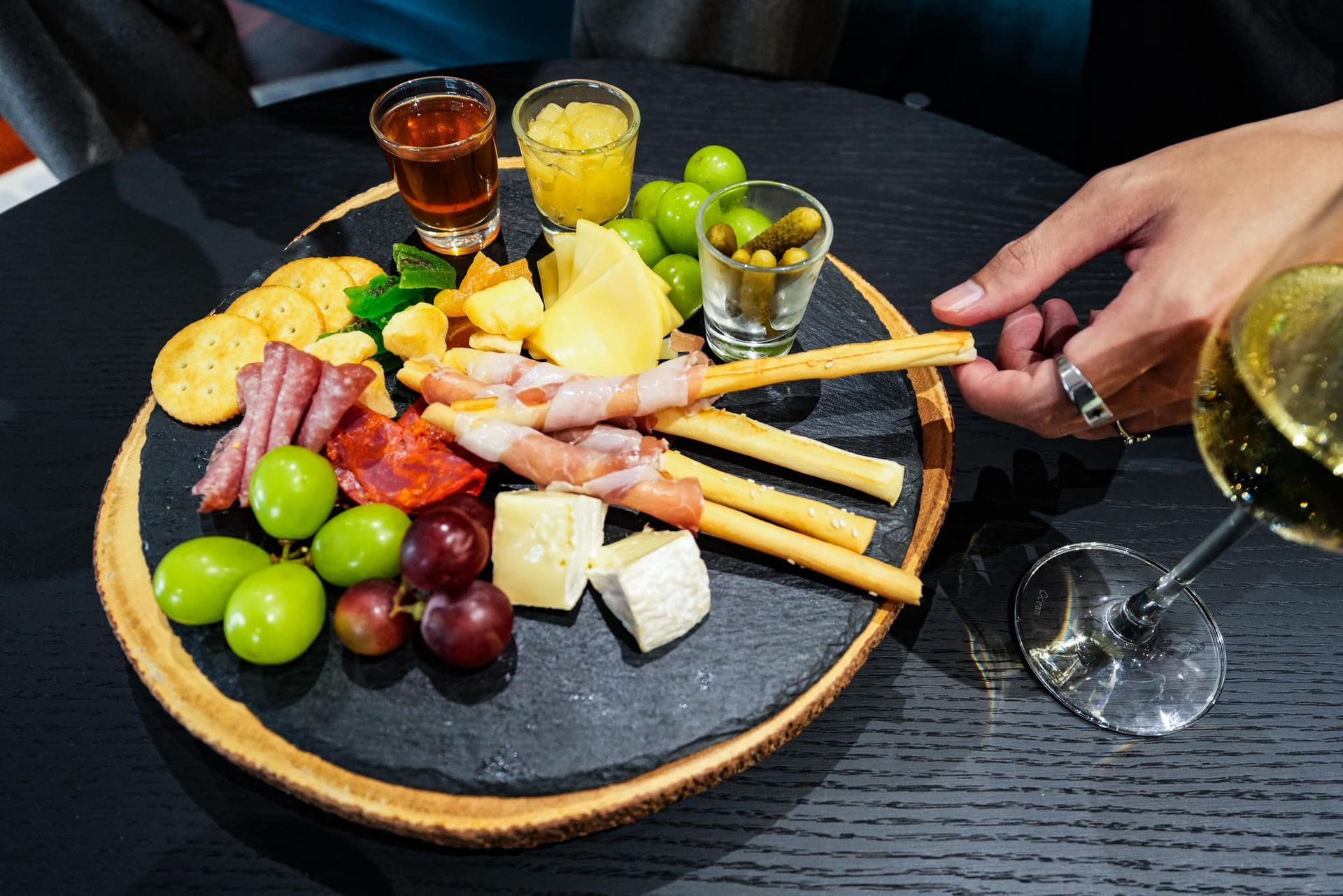 A person is holding a glass of wine next to a plate of food.