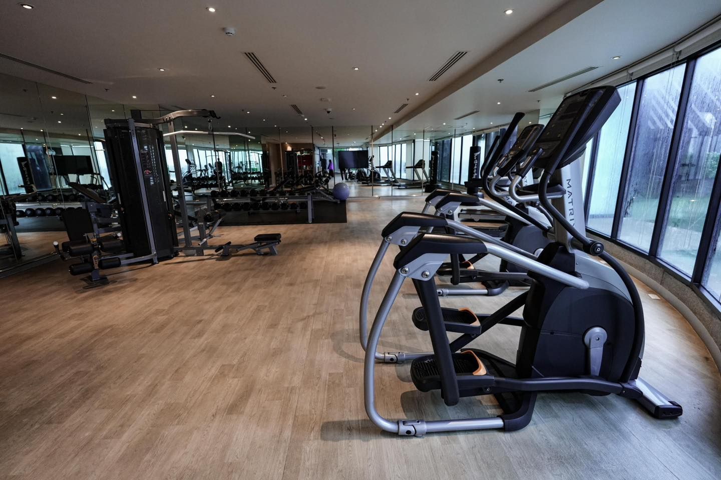 A gym with a lot of exercise equipment and a lot of windows.