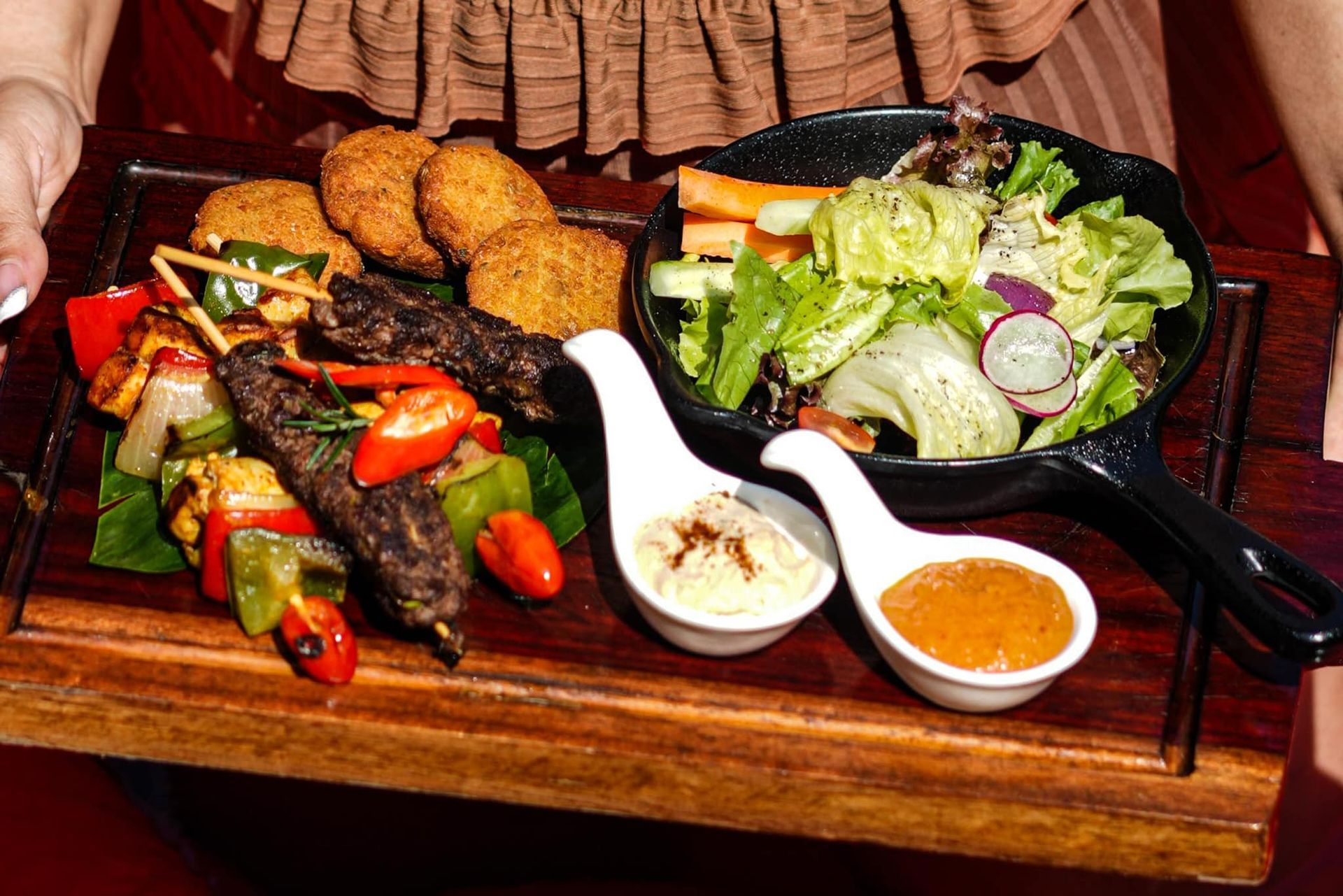 A person is holding a wooden tray with food on it