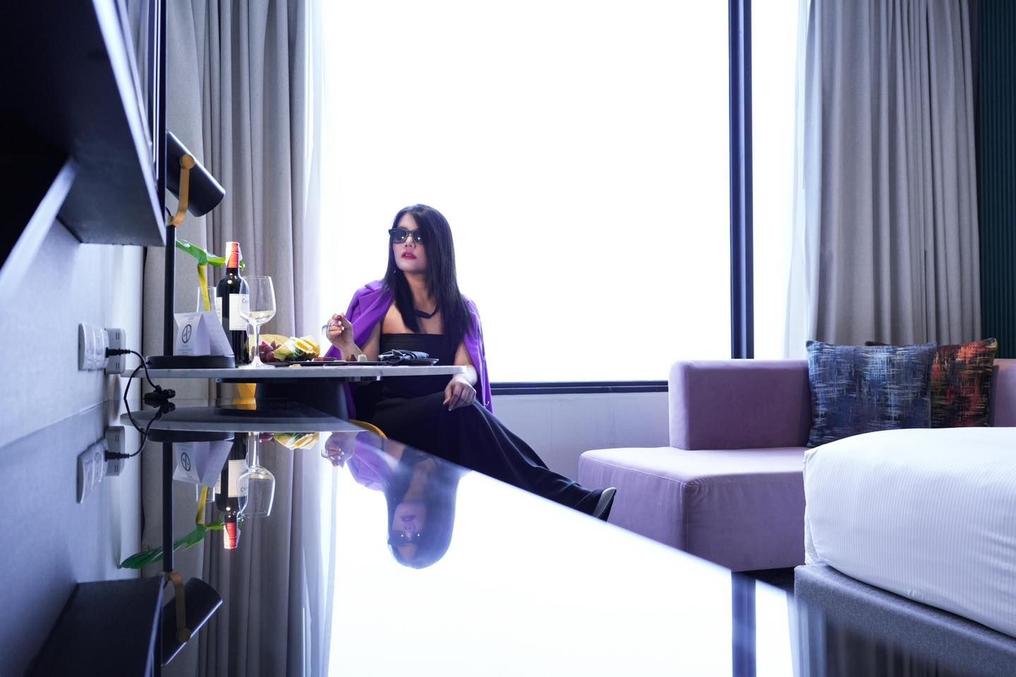A woman is sitting at a table in front of a window in Avani Sukhumvit  hotel room.