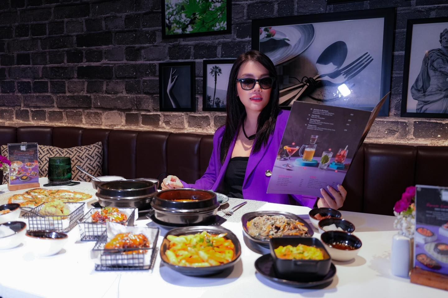 A woman is sitting at a table with plates of food and a menu.