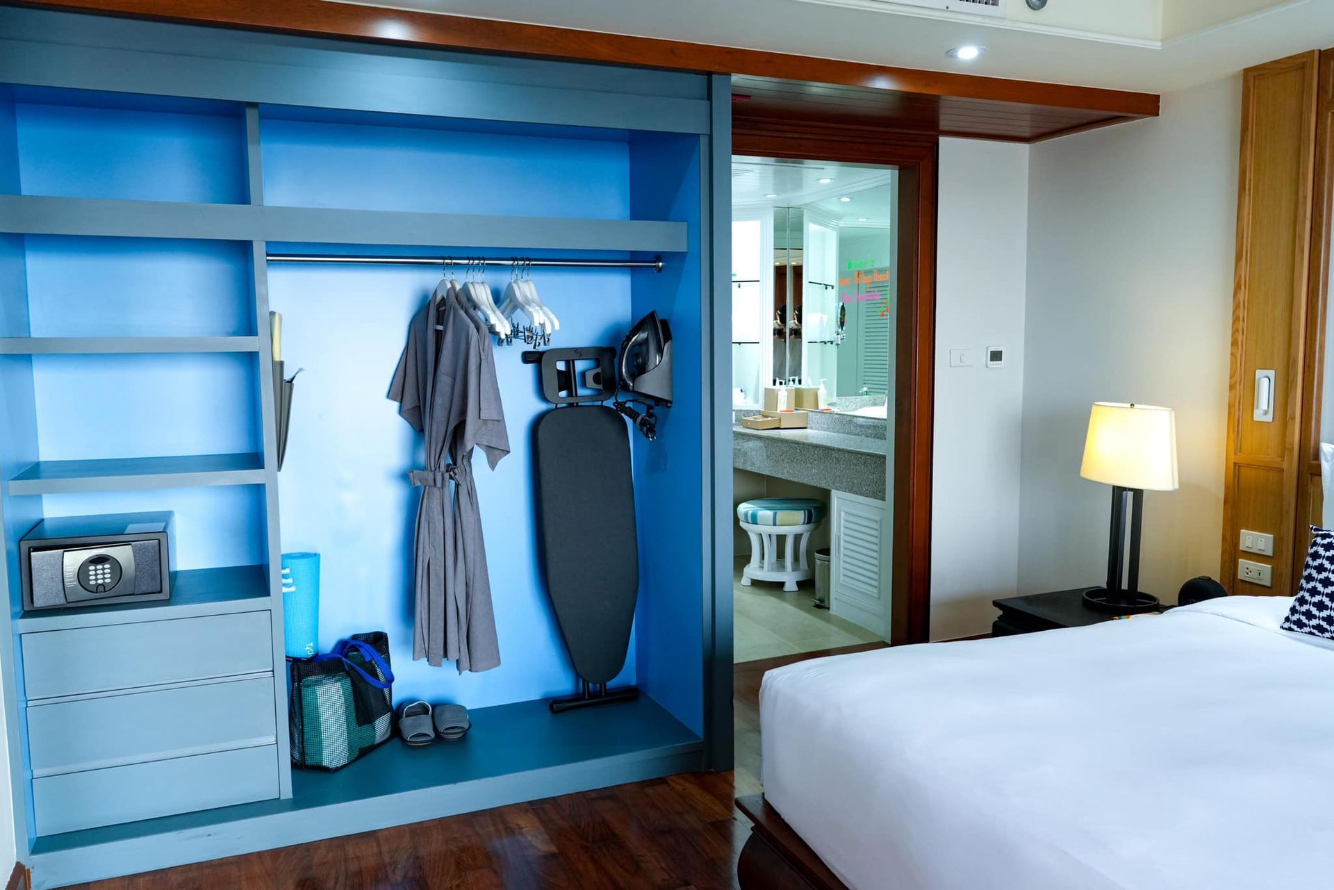 A hotel room with a bed , closet , and ironing board.