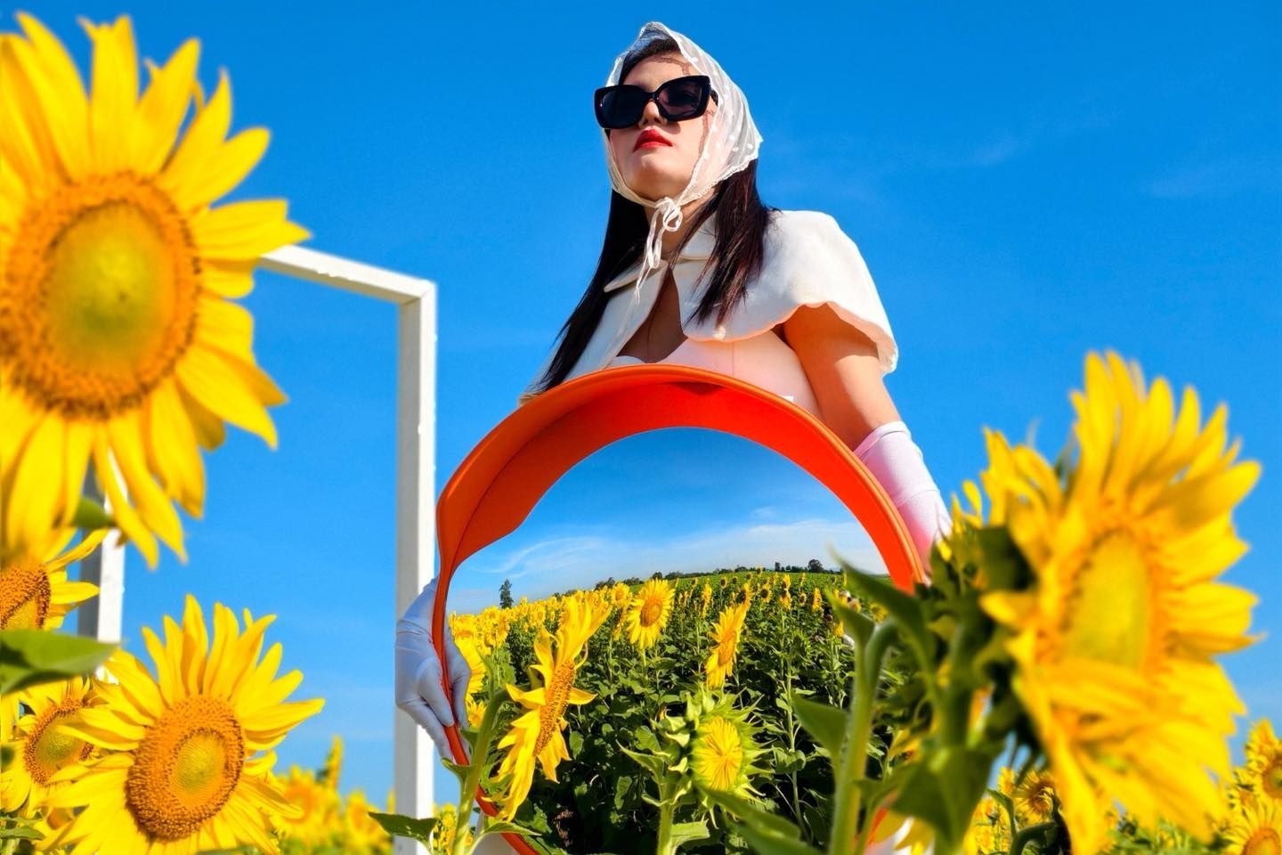 A woman is standing in a field of sunflowers holding an orange ring.