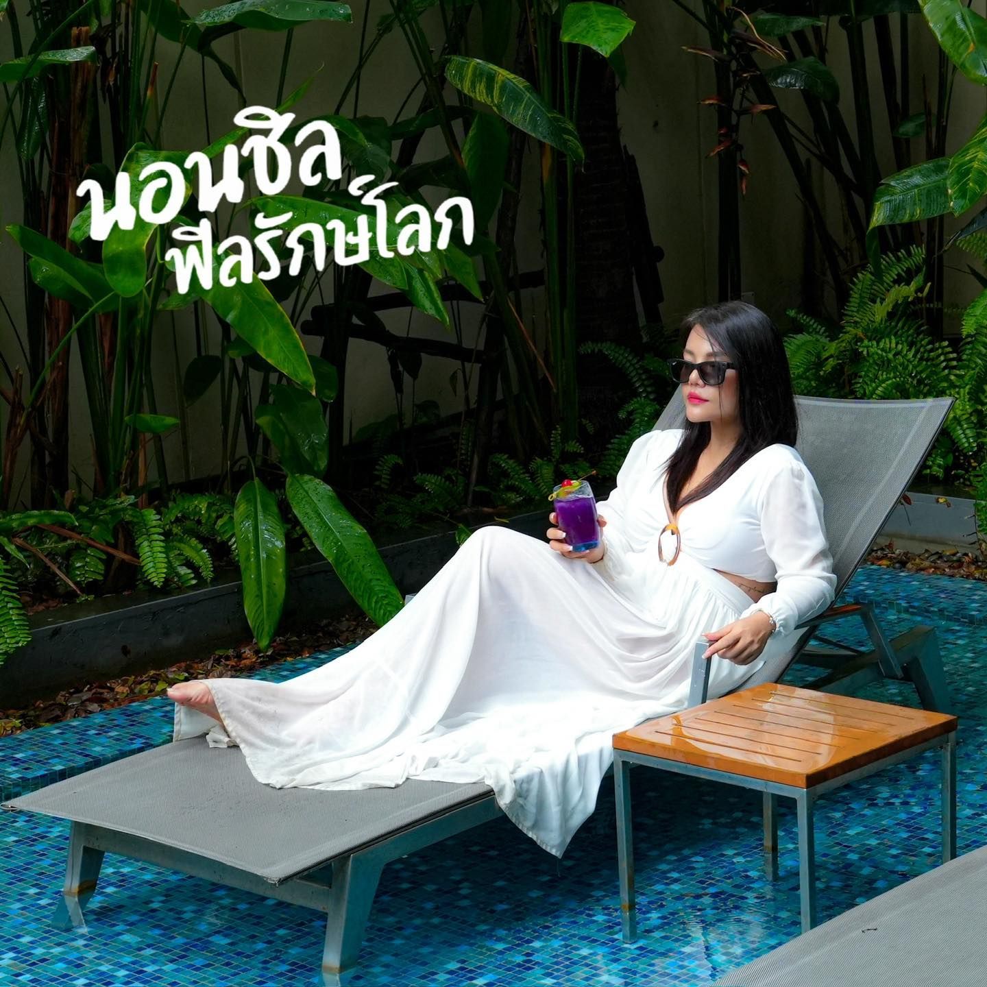 A woman in a white dress is sitting on a lounge chair in a pool holding a drink.