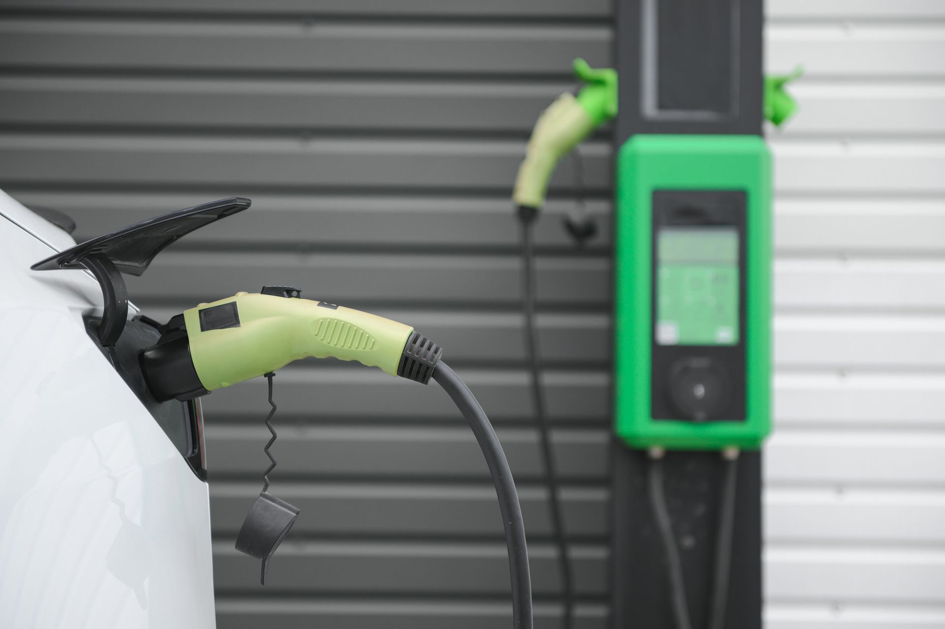 Electric vehicle charging cable plugged into a white car at a green charging station