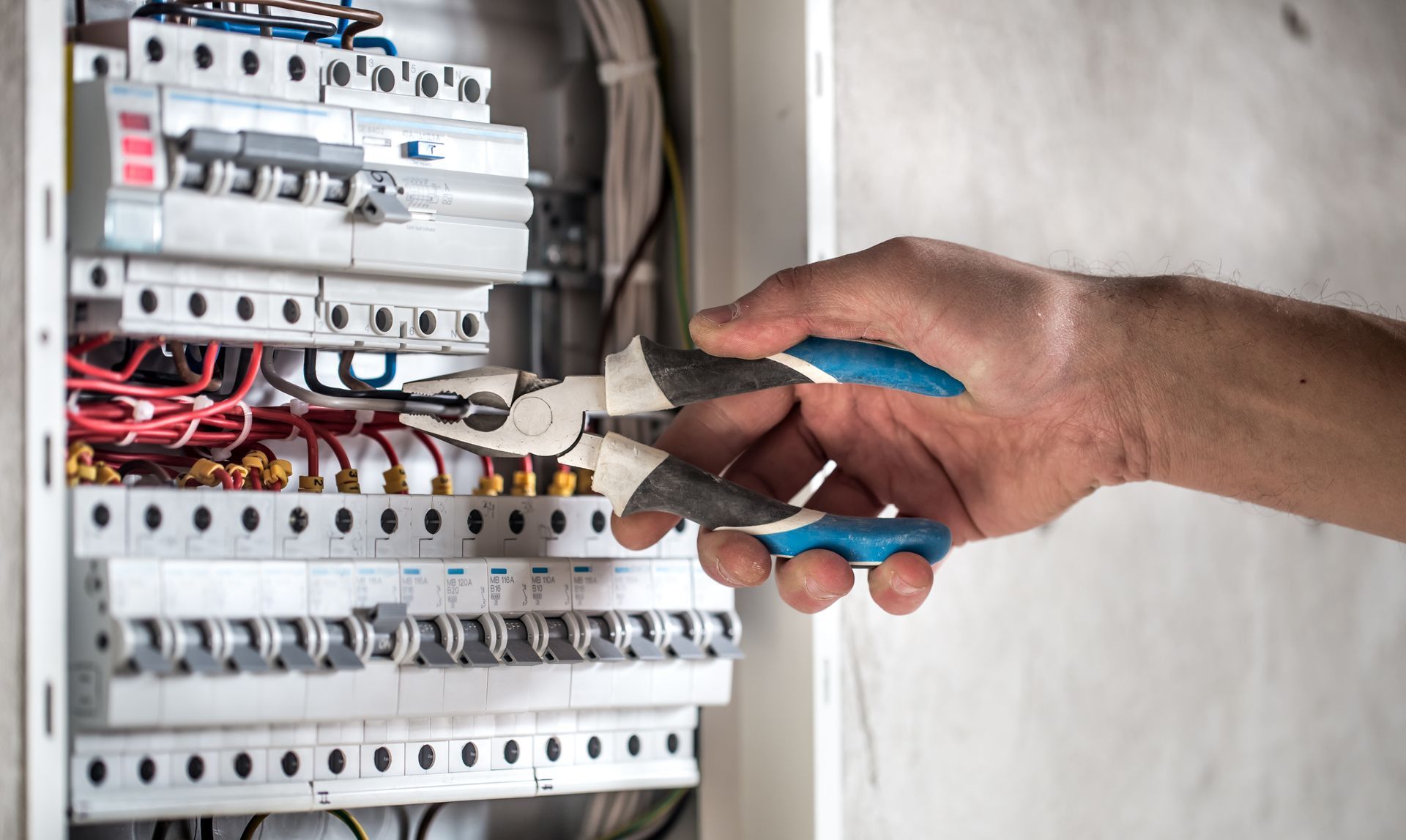 A person is working on an electrical box with a pair of pliers.